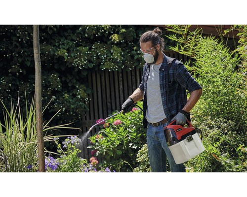 Man med skyddsglasögon och andningsmask som använder en batteridriven växtspruta i trädgården.