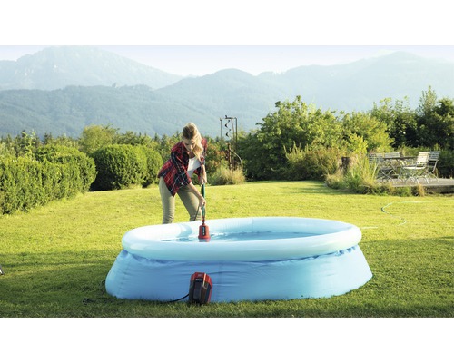 Kvinna använder en dränkbar pump för att ta bort vatten från en uppblåsbar pool i trädgården.
