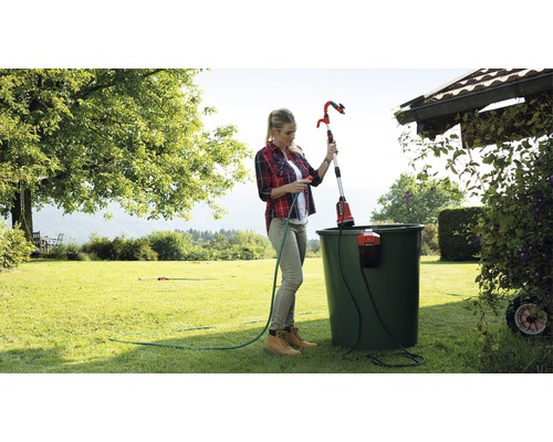 Kvinna använder en teleskopisk trädgårdssprinkler för att vattna växter i trädgården.