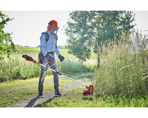 Man klipper gräs med en batteridriven grästrimmer i trädgården.