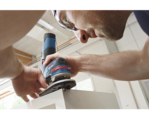 Man med skyddsglasögon använder en handöverfräs på ett arbetsstycke.