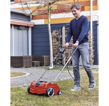 En man använder en elektrisk mossrivare i trädgården för att sköta gräsmattan.