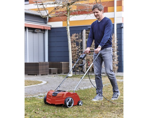 En man använder en elektrisk mossrivare i trädgården för att sköta gräsmattan.