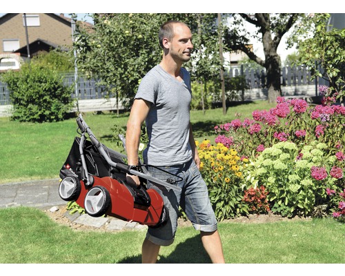 En person bär en gräsmattluftare genom en trädgård.