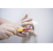 En hand utför elarbeten med en skruvmejsel på ett eluttag.