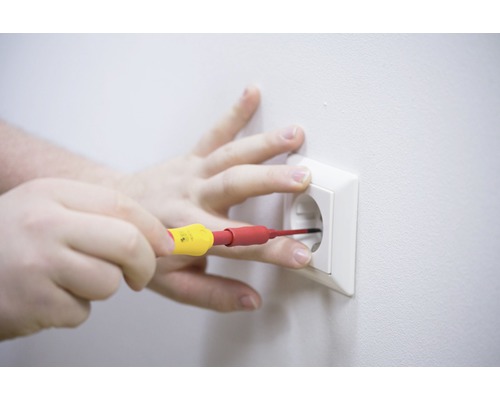 En hand utför elarbeten med en skruvmejsel på ett eluttag.