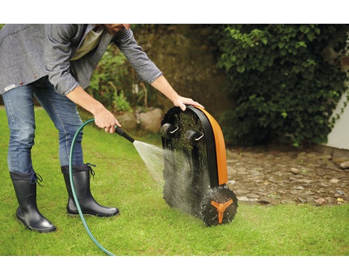 En man rengör en robotgräsklippare med en vattenslang på en gräsmatta.