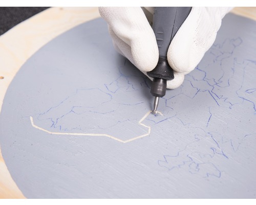 En hand med handske använder ett multifunktionsverktyg på en målad träcirkel.