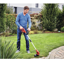 Man klipper gräsmattans kanter med en batteridriven grästrimmer i trädgården.