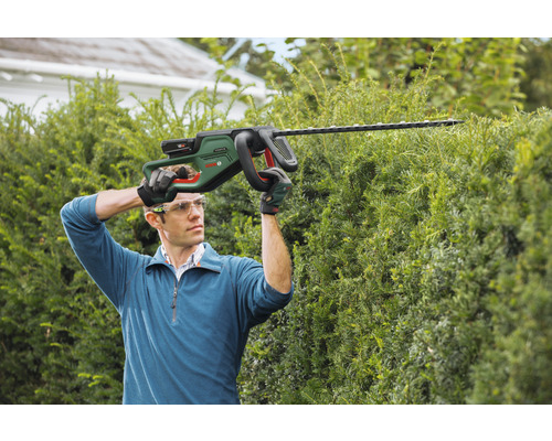 Man klipper häck med en batteridriven häcksax.