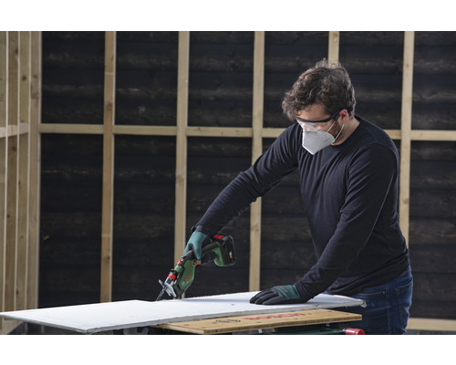 En person sågar en gipsskiva med en sladdlös tigersåg. Skyddsutrustning används.