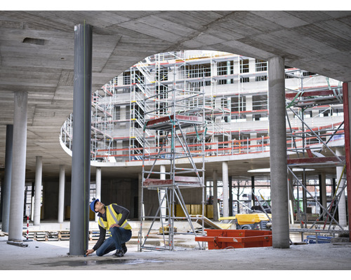 Byggnadsarbetare mäter en stålstolpe på en byggarbetsplats.