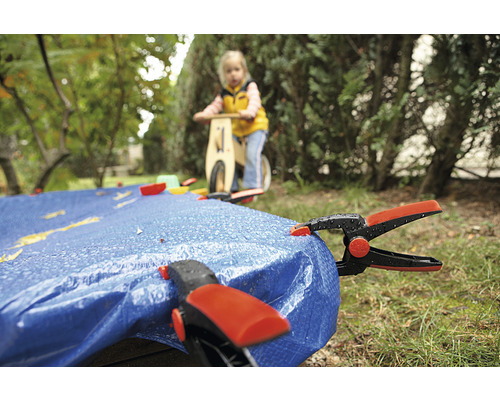 Täckande presenning med klämmor i trädgården, barn på springcykel i bakgrunden