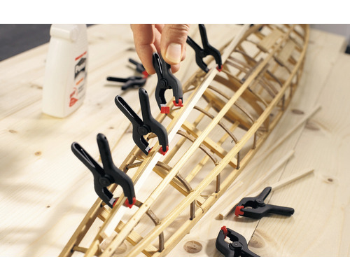 Modellbygge av en båtskrov med fjäderklämmor på en träyta