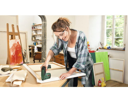 Kvinna spänner duk med en elektrisk häftpistol i en ljus ateljé