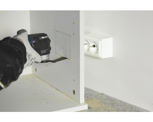 En person skär ett hål i en träbit med ett multifunktionsverktyg nära ett eluttag.