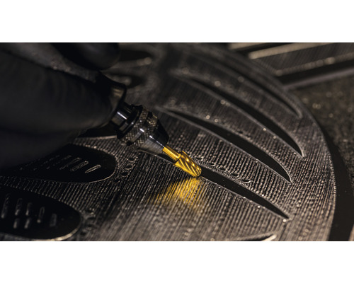 Närbild av en hand med en gravyrstickel som graverar detaljer i ett arbetsstycke.