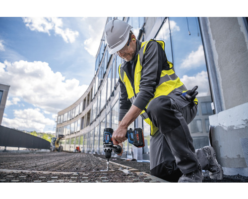 En byggnadsarbetare knäböjer och använder en sladdlös skruvdragare på en byggarbetsplats.
