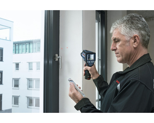 Man använder en värmekamera för att analysera ett fönster.