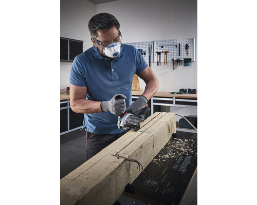 En hantverkare med skyddsglasögon och andningsskydd sågar i en träbit med en spårfräs.