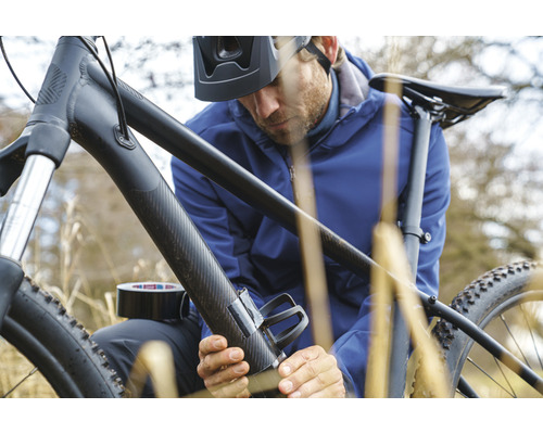Man fäster en flaskhållare på en cykel med silvertejp.
