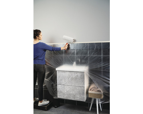 Kvinna målar en vägg med en färgroller i ett badrum som är täckt med plastfilm