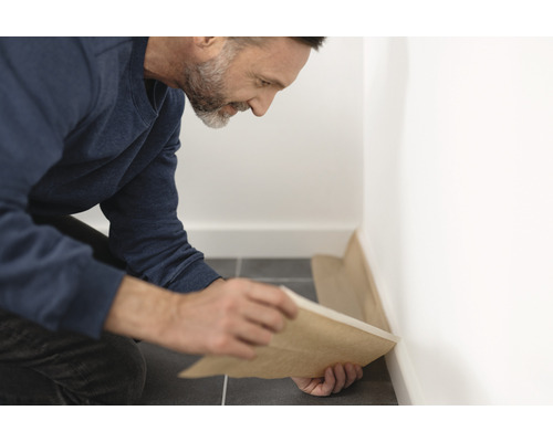 Hantverkare lägger skyddsfilm längs en vägg på ett klinkergolv.