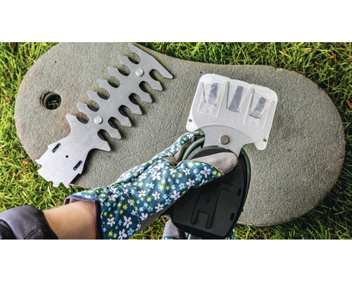 En hand med trädgårdshandske håller en häcksaxslipare, bredvid en anordning för att rikta in häcksaxar