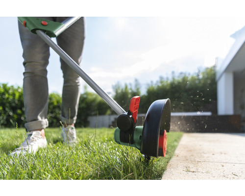 Person trimmar gräs med grästrimmer vid trädgårdsgång