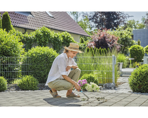 Kvinna tar bort ogräs med en fogskrapa på en stenlagd terrass.