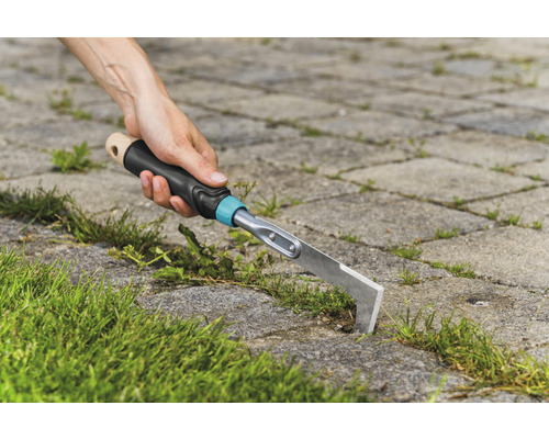 Person som tar bort ogräs mellan stenplattor med en fogskrapa.