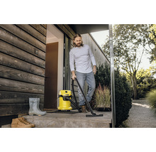 Man rengör en terrass framför ett hus med en våt- och torrdammsugare. I bakgrunden syns växter.