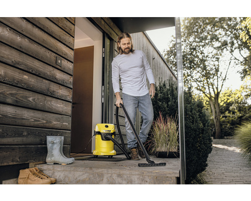 Man rengör en terrass framför ett hus med en våt- och torrdammsugare. I bakgrunden syns växter.