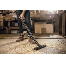 En person dammsuger upp träflis med en dammsugare.