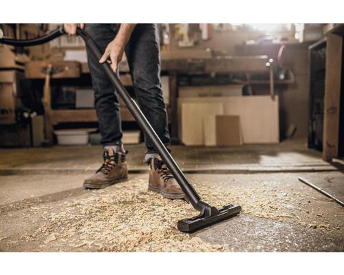 En person dammsuger upp träflis med en dammsugare.