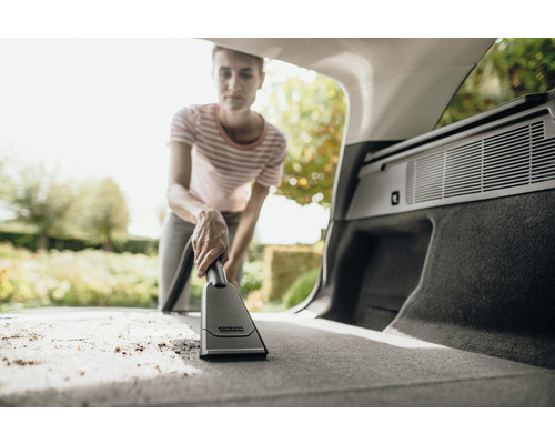 Kvinna dammsuger bagageutrymmet på en bil med en Kärcher dammsugare.