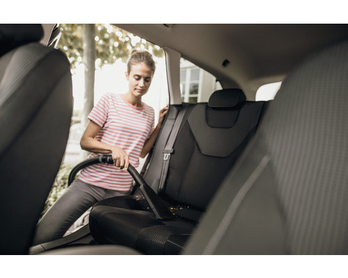 Kvinna dammsuger bilsäten med en dammsugare.