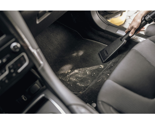 En person dammsuger det smutsiga fotutrymmet i en bil med en dammsugare.