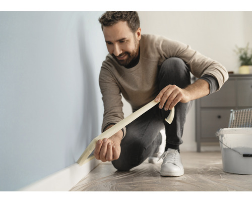 En man fäster maskeringstejp på en vägg i ett rum.