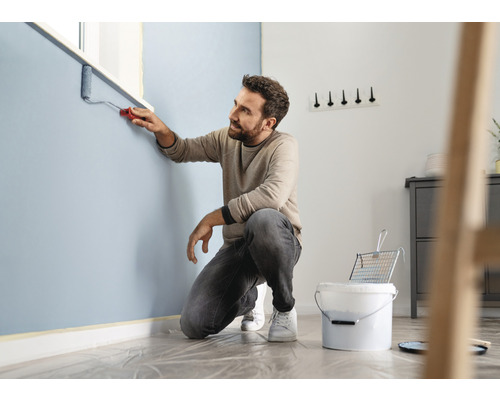 Man målar vägg med roller i ett rum