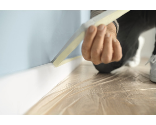 En person sätter maskeringstejp på en vägg med golvsockel för att skydda den från färgstänk.