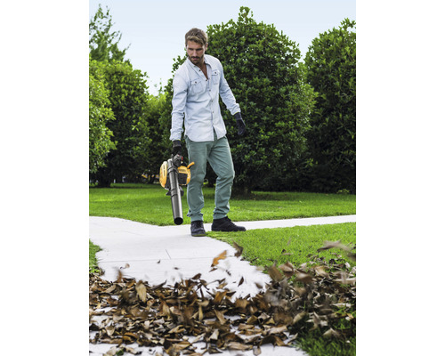 Man använder en gul lövsug i trädgården för att ta bort löv.