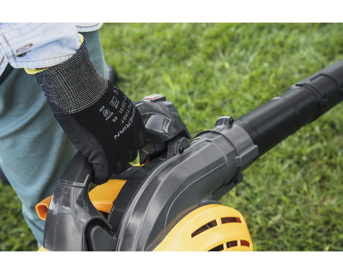 En person använder en lövsug i trädgården och bär handskar.