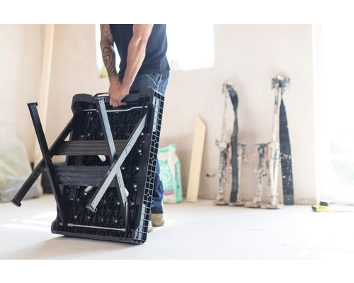 En person bär en hopfälld arbetsplattform i ett rum.