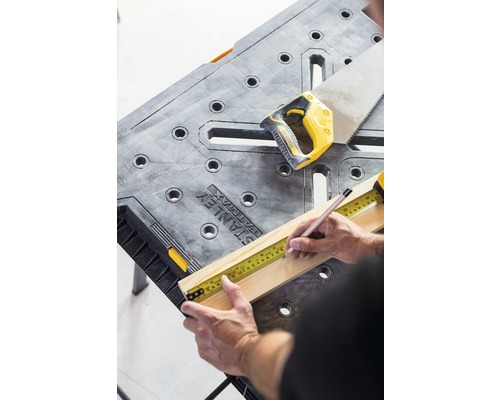 Man mäter träplanka med måttband på en arbetsbänk, bredvid en handsåg