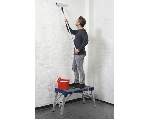 Man målar en vägg med en färgrulle från en arbetsplattform.