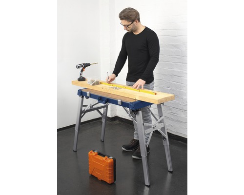 Man arbetar med en arbetsbänk, en batteridriven skruvdragare, skruvar och ett måttband på en träplanka.