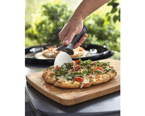 En pizza skärs med en pizzaslicer på en skärbräda.