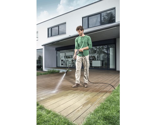 Man rengör träterrass med högtryckstvätt framför ett hus.