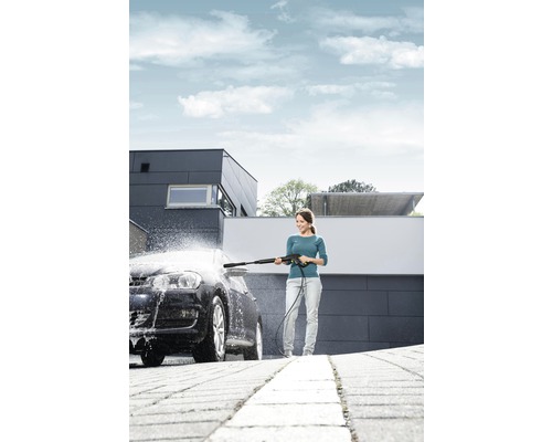 Kvinna rengör bil med högtryckstvätt framför hus